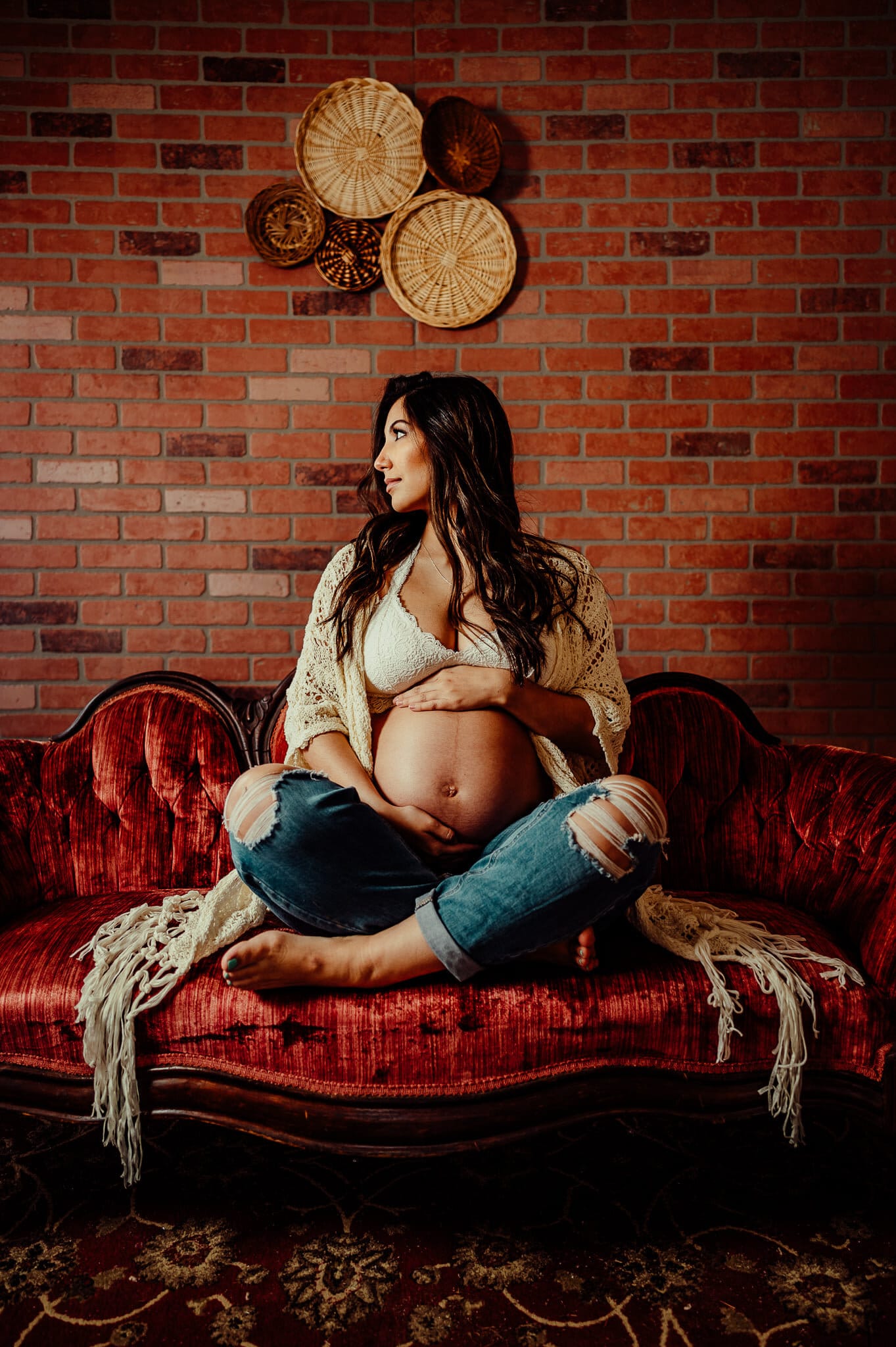 Woman sitting on red antique couch for maternity photos