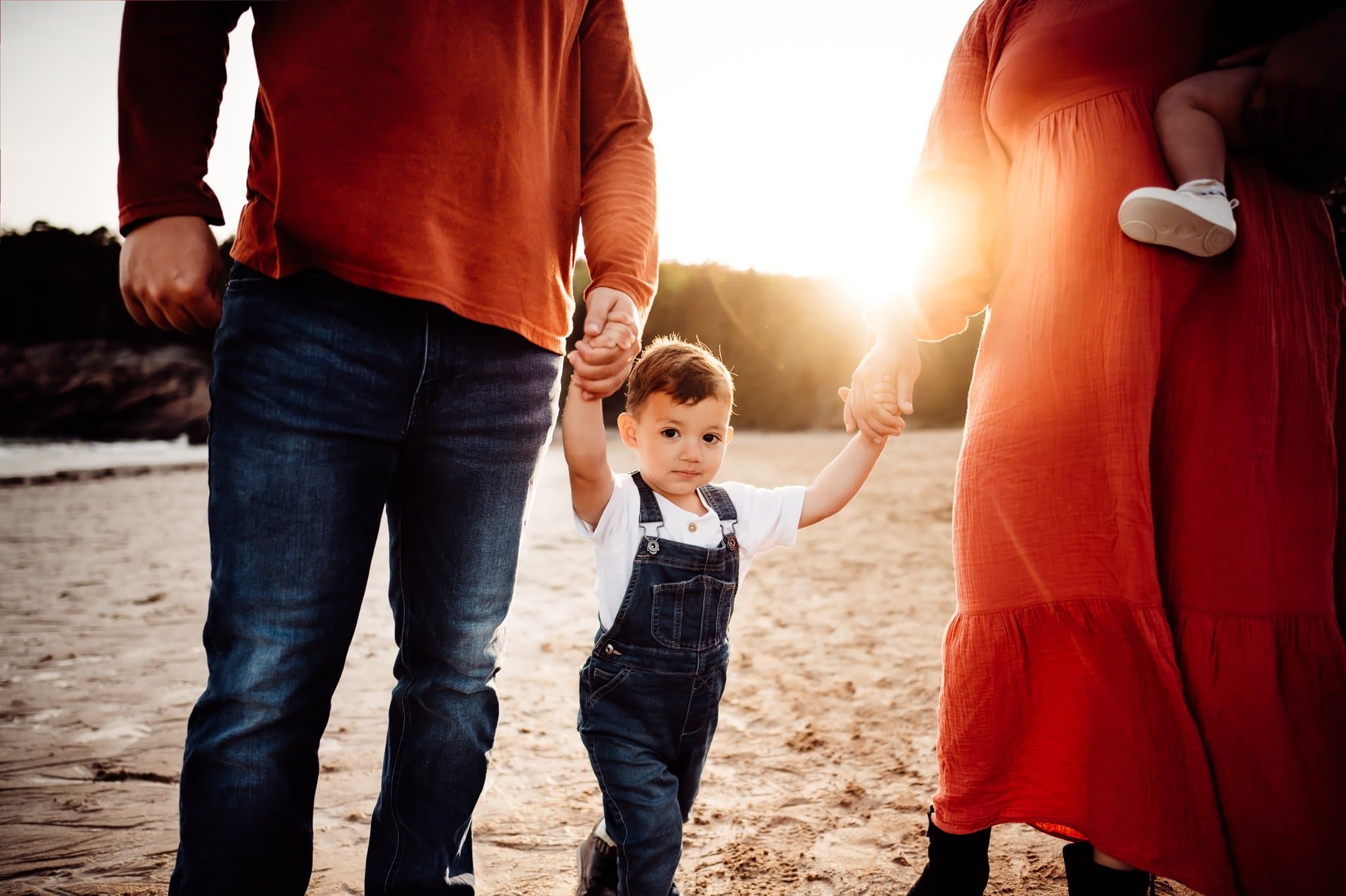 Little boy looking at camera holding mom and dads hands