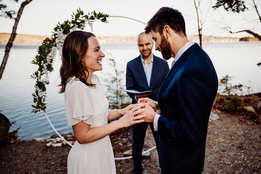 Groom putting wedding ring on bride in front of lake