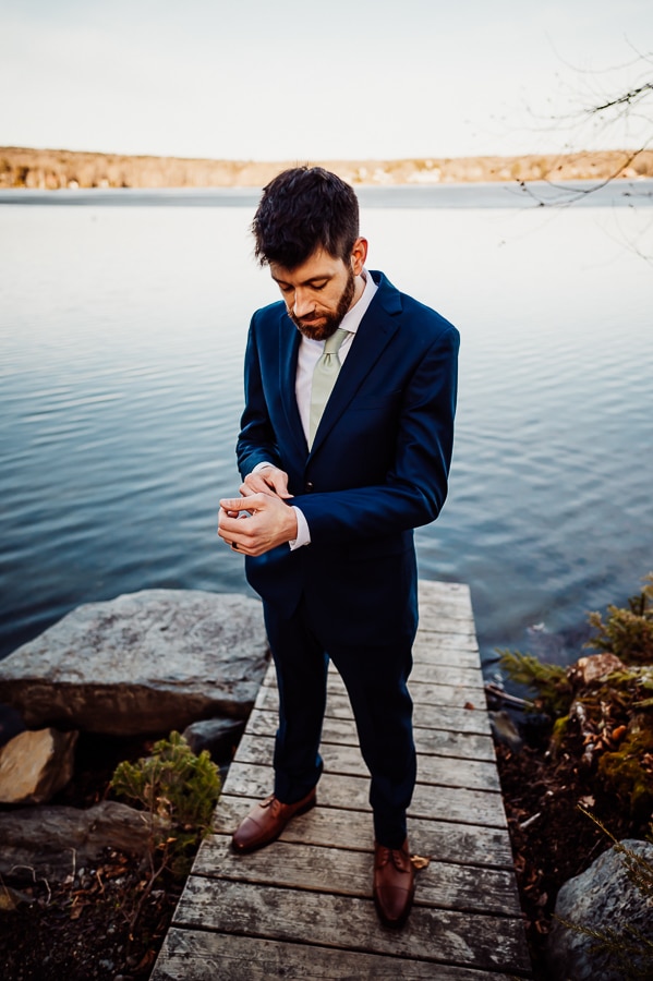 groom adjusting cuff links in front of lake