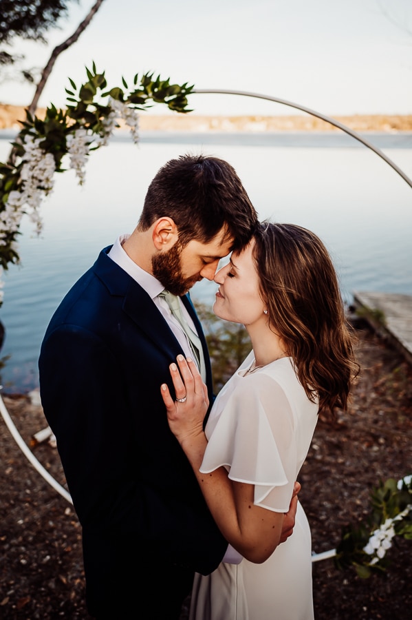 Bride and groom touching foreheads in front of lake