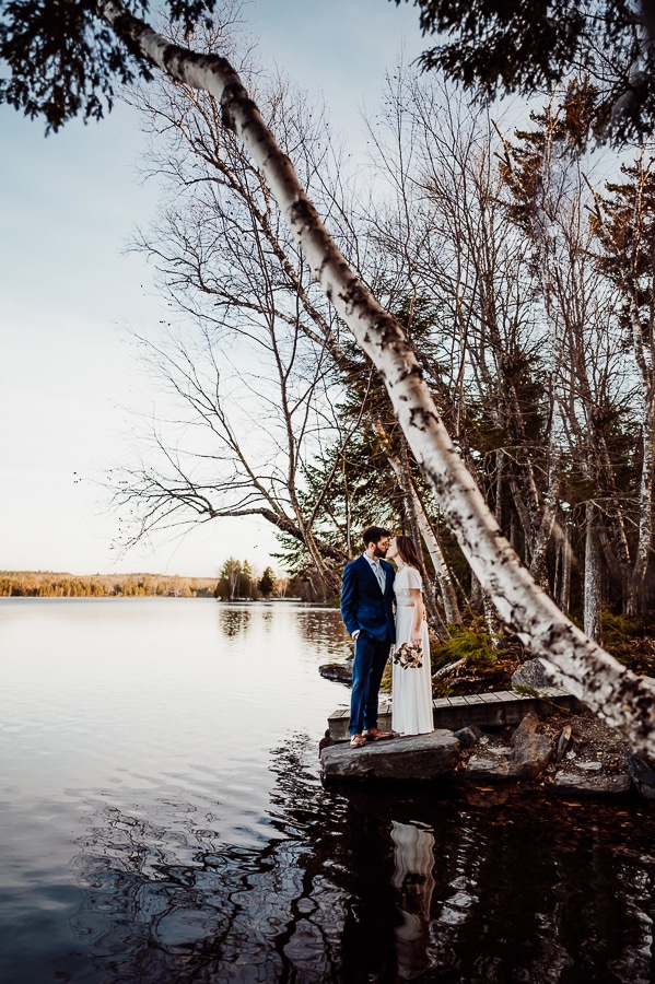 Bride and groom standing on edge of moosehead lake in greenville
