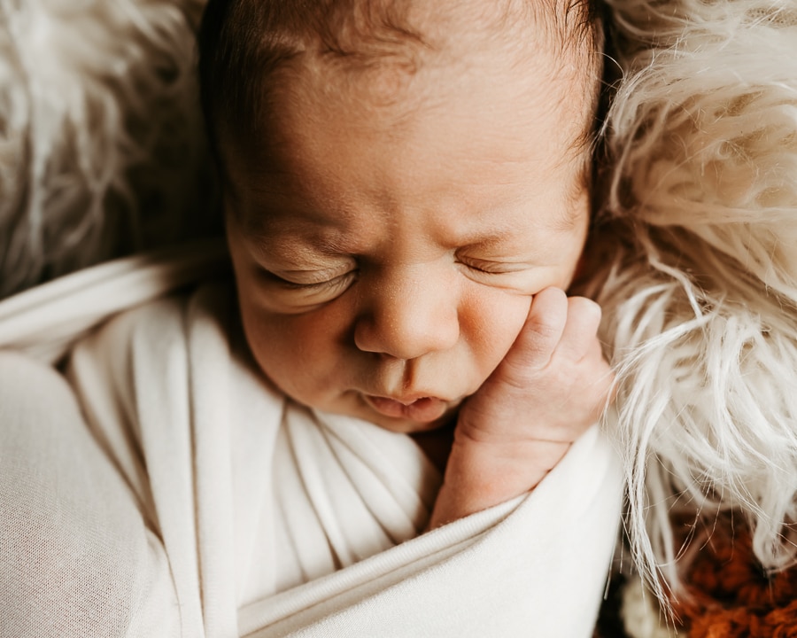 Newborn baby scrunched face with hand on cheek