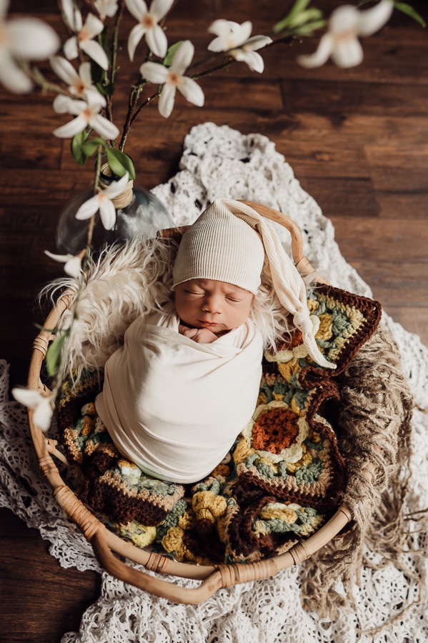 Newborn baby wrapped in basket with afghan blanket and sleepy hat