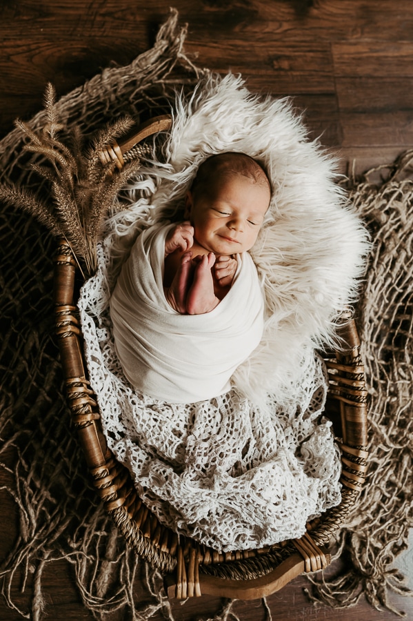 Newborn Baby wrapped in white wrap in basket with furr