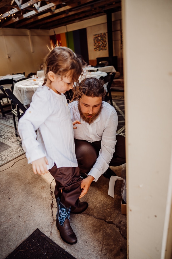 Groom helping son put on boots at wedding