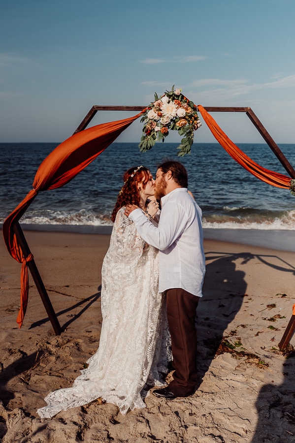 Bride and groom kissing at alter on beach