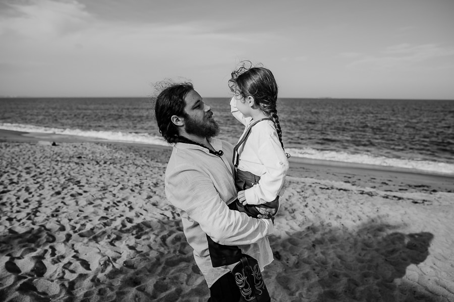 Black and white Groom holding son on beach