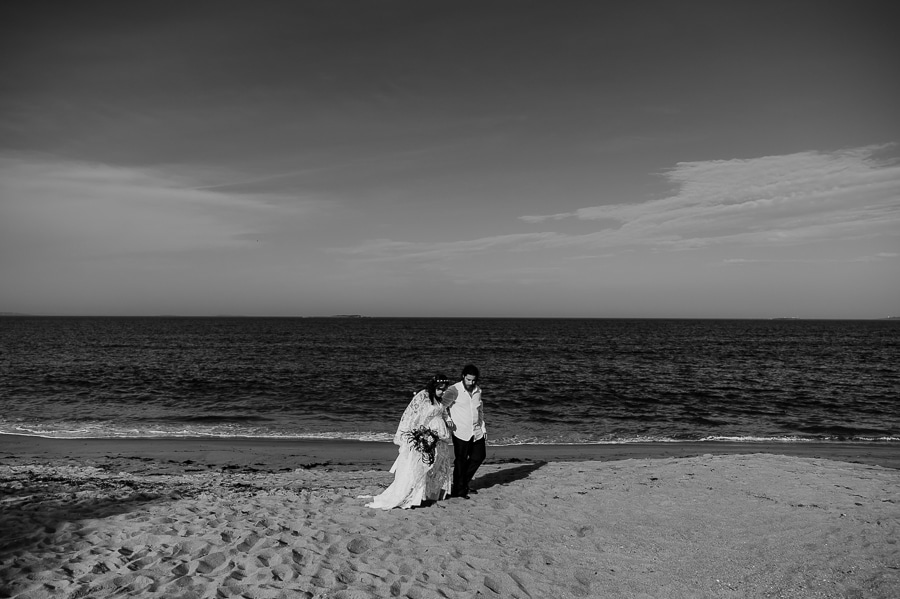 Black and white bride and groom walking on beach looking at each other