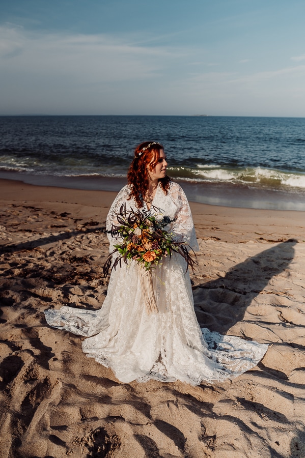 Bride on old orchard beach holding flowers in front of the ocean