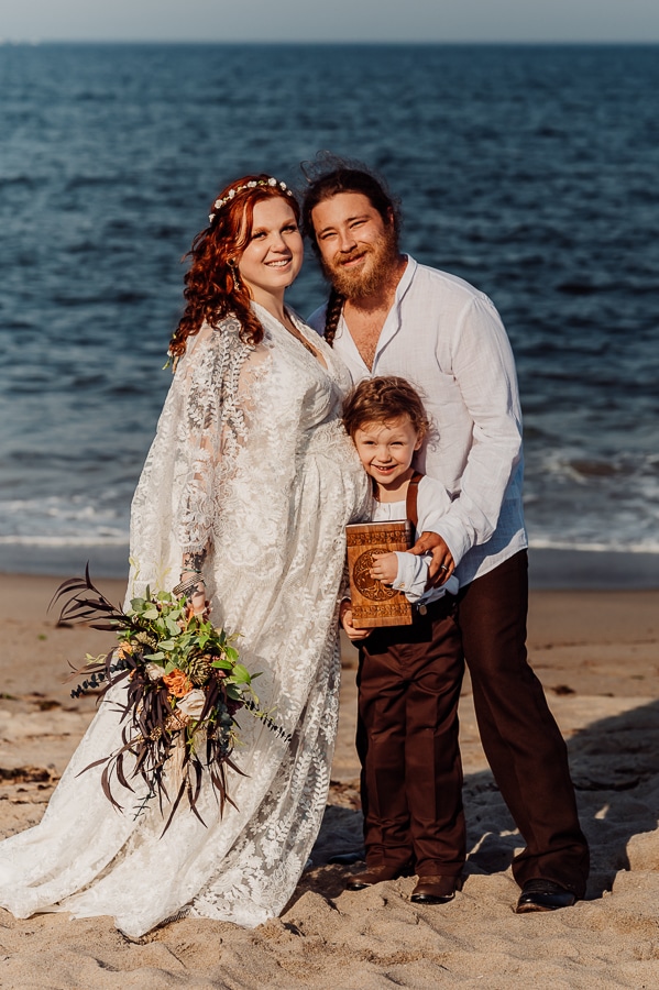 Bride and groom posing on beach with son and baby's urn