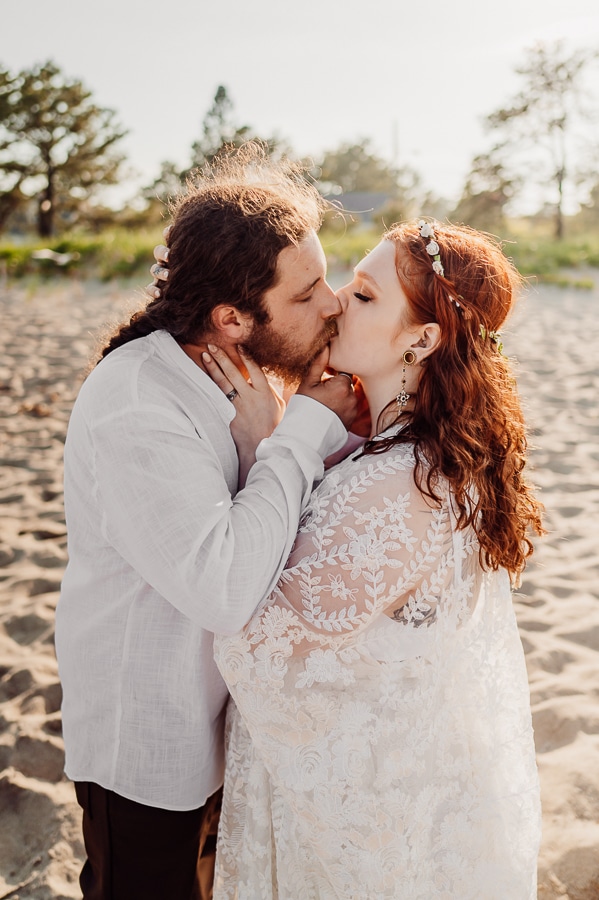 bride with red hair kissing groom on beach
