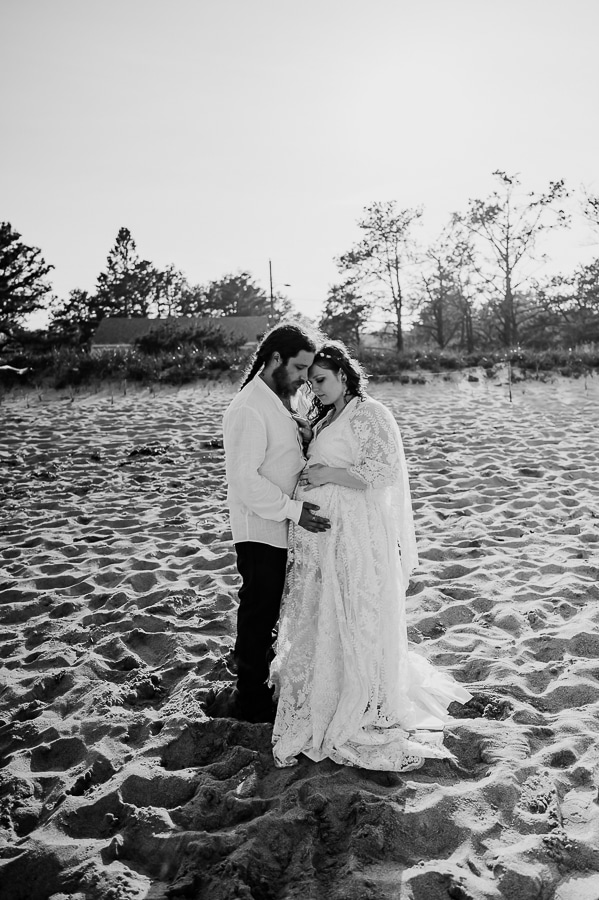 Black and white bride and groom posing and holding belly on beach