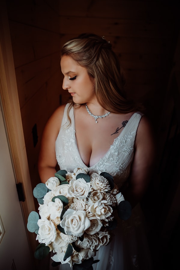Bride looking down while holding flowers by window