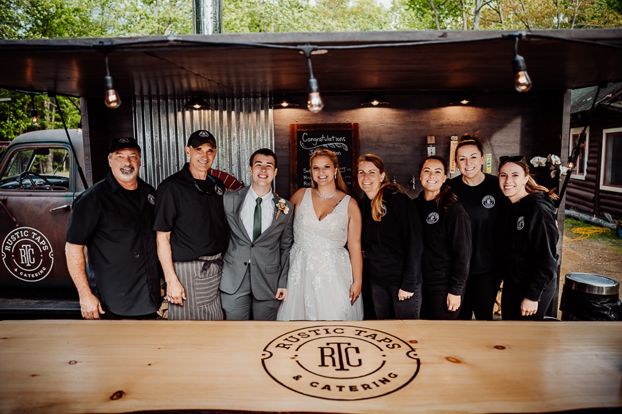 Bride and groom posing with catering crew rustic taps