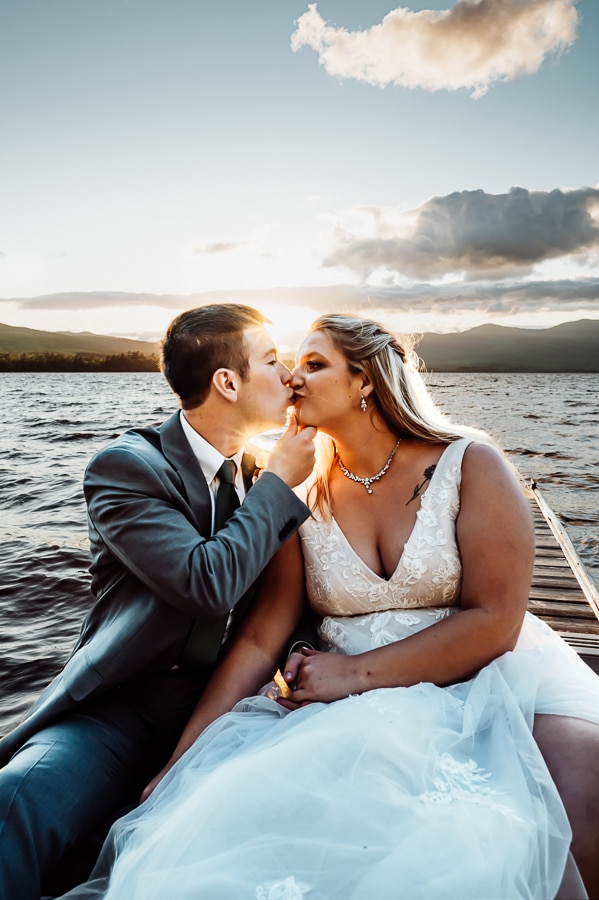 Groom pinching brides chin and kissing on the lake at sunset