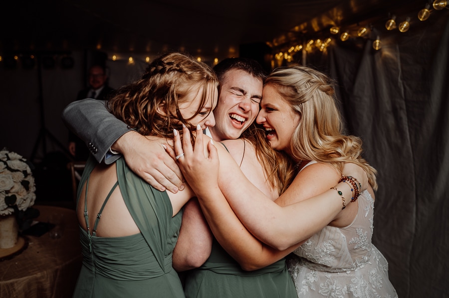 Bride and groom hugging group of friends crying after wedding speech