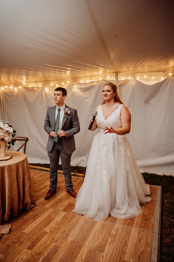 Bride and groom giving speech at wedding reception in tent