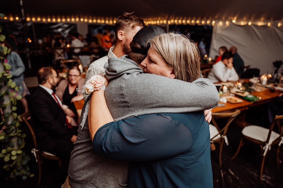 Woman in blue dress hugging friend in grey sweatshirt at wedding reception