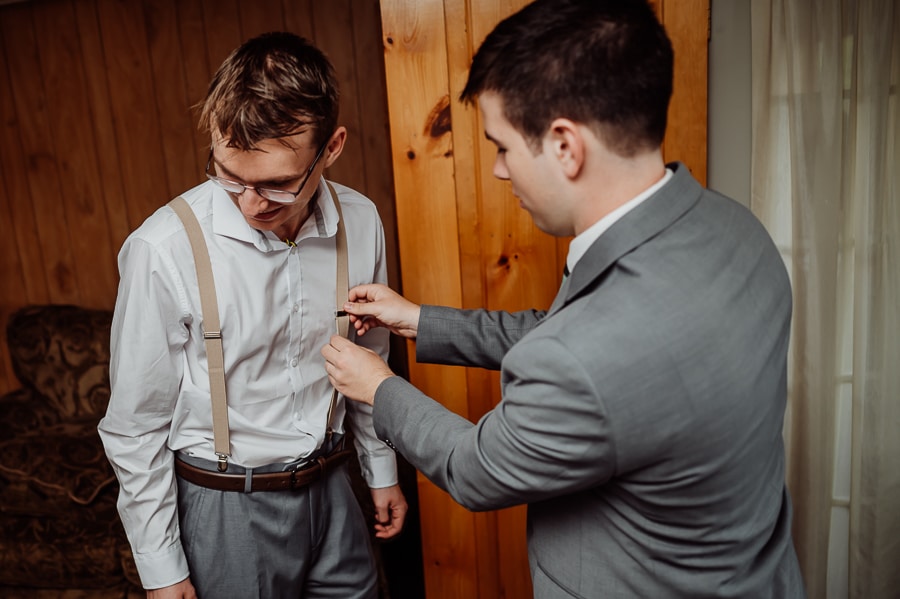 Groom fixing groomsmen's suspenders before wedding