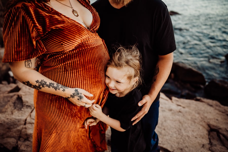 Family embracing pregnant belly on maine coast