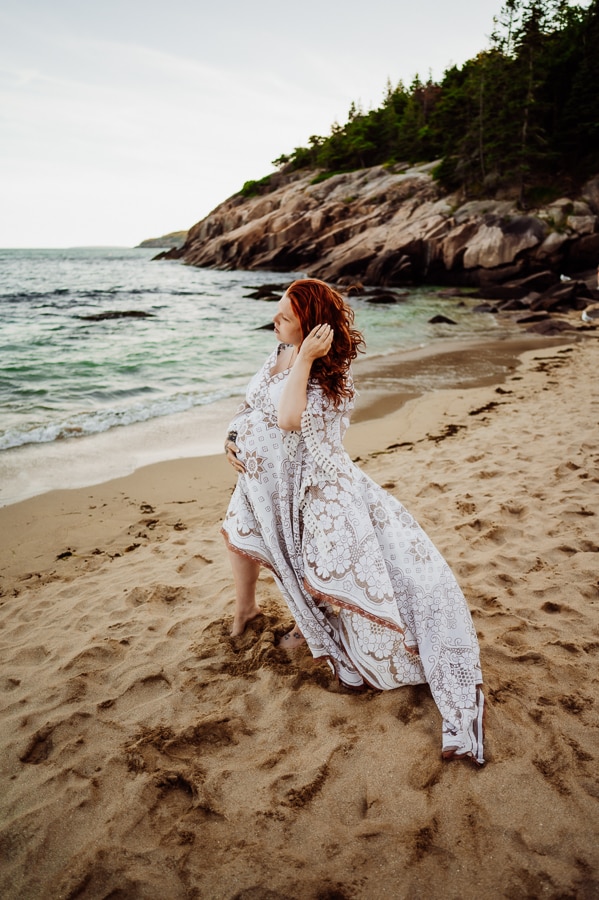 Pregnant woman playing with hair in white dress on beach