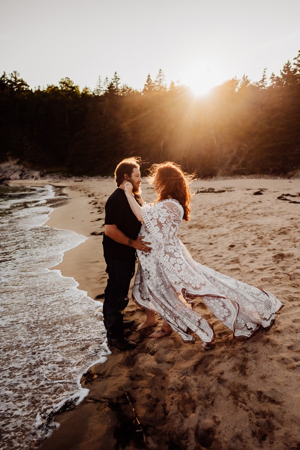 Pregnant woman and husband on sand beach in white dress