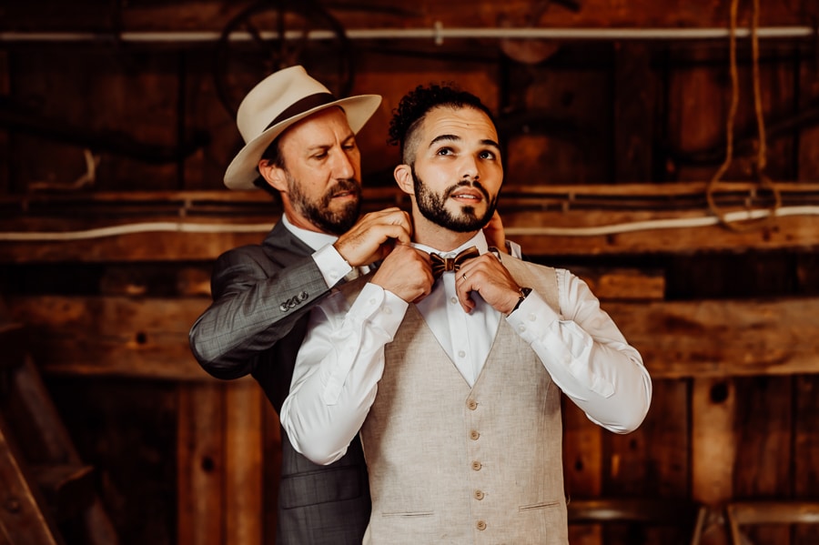 Father helping son put on tie before wedding in barn