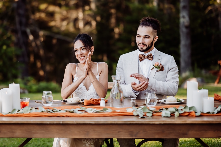 Bride and groom sitting at head table outside clapping after wedding speech