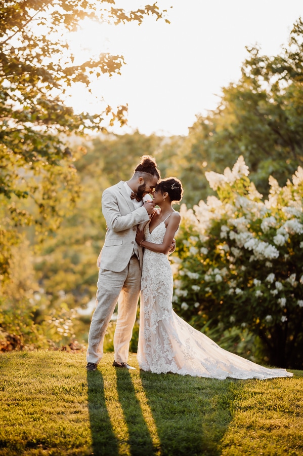 Groom pinching brides chin and kissing in front of flowers and bushes at sunset