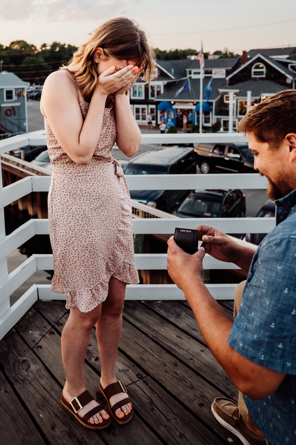 Woman holding hands over her face as she is proposed to on bridge