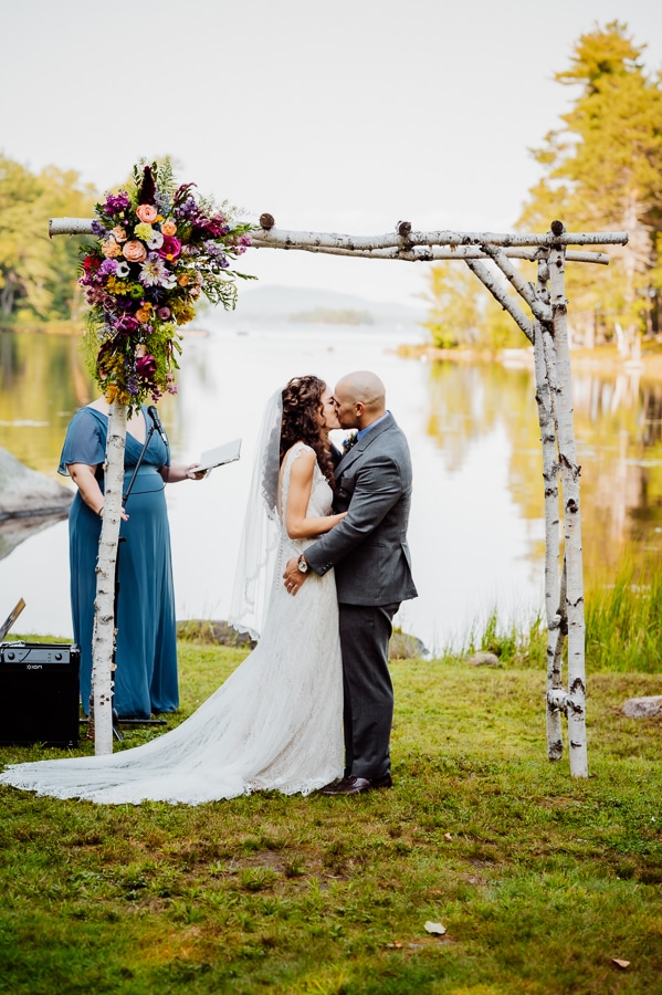 Bride and groom first kiss in front of millinocket lake at big moose inn
