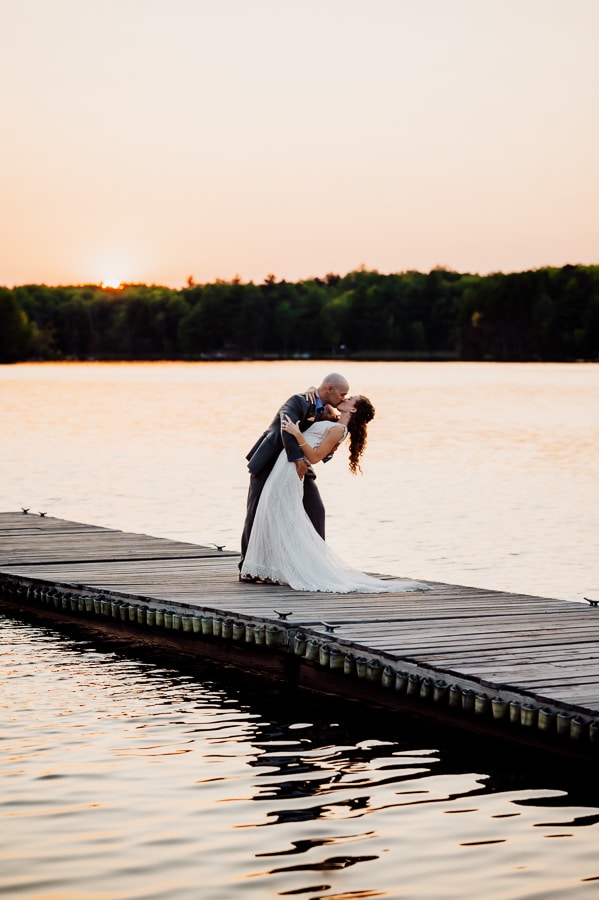 Bride and groom kissing on dock at sunset at big moose inn