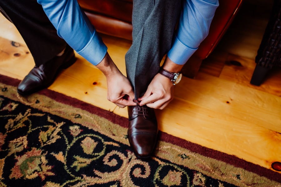 Groom tying shoes on wood floor and rug
