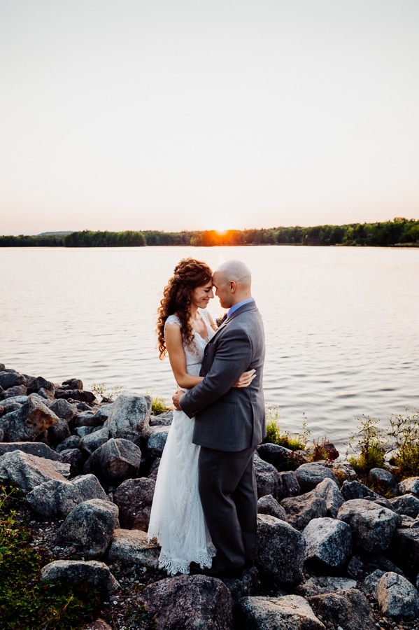 Bride and groom on rocks in front of lake at sunset at big moose inn