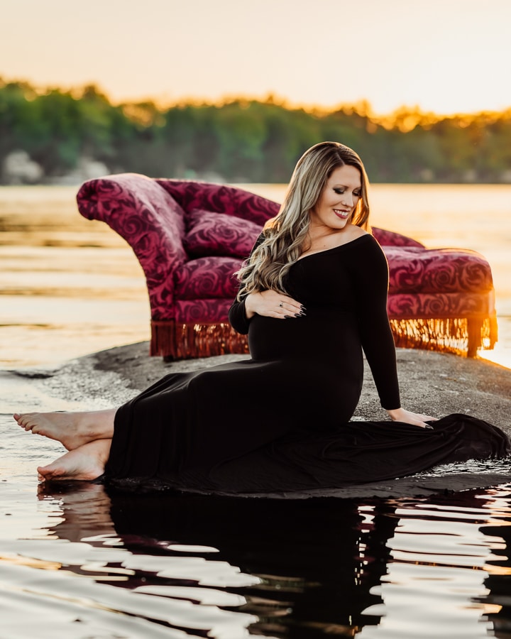 Woman wearing black dress sitting on rock in lake in front of antique couch