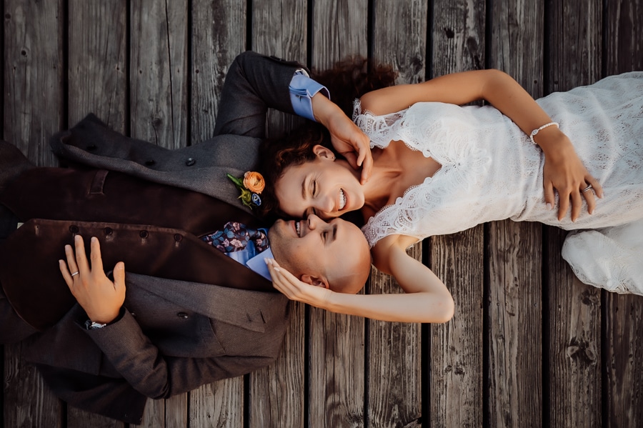 Bride and groom laying on dock with faces together