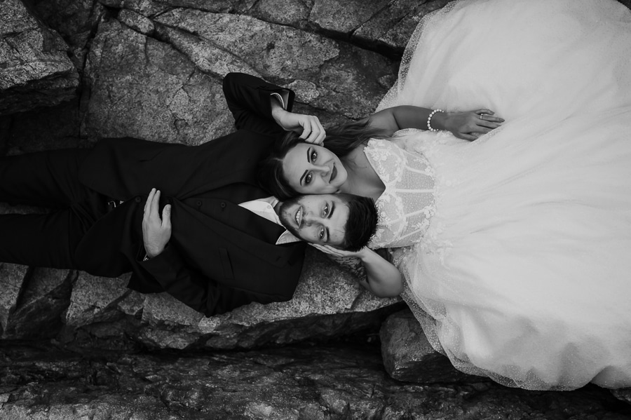Bride and groom laying down together on rocky cliff in black and white
