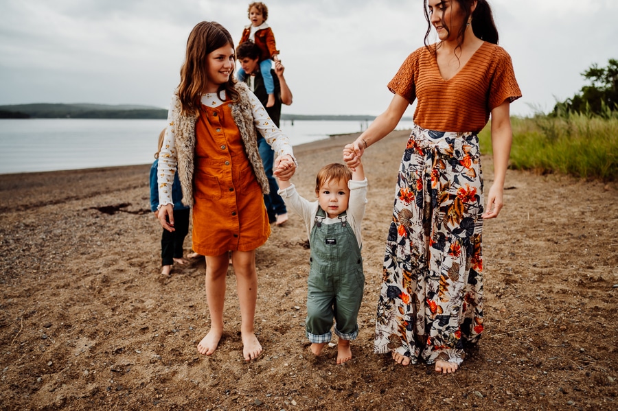 Mother and daughter wearing orange holding hands with little boy wearing green overalls at beach