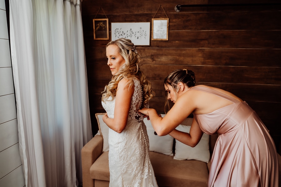 Bridesmaid helping fasten buttons on wedding dress with bride