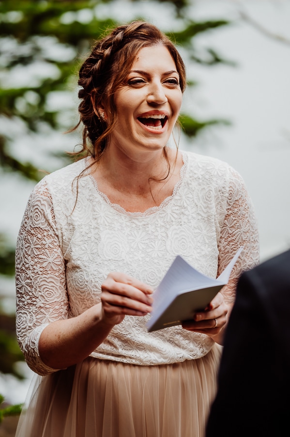 bride smiling and laughing while holding vow book during ceremony