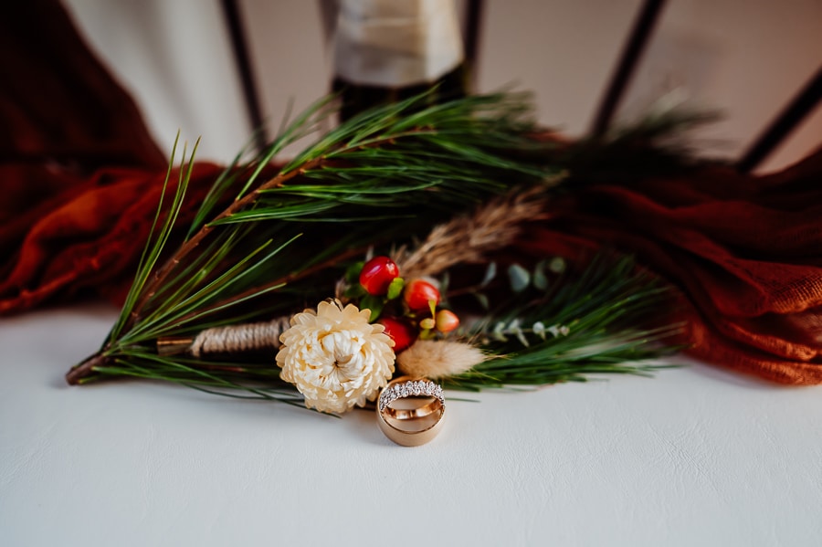 Wedding rings in front of boutonniere and pine branch 