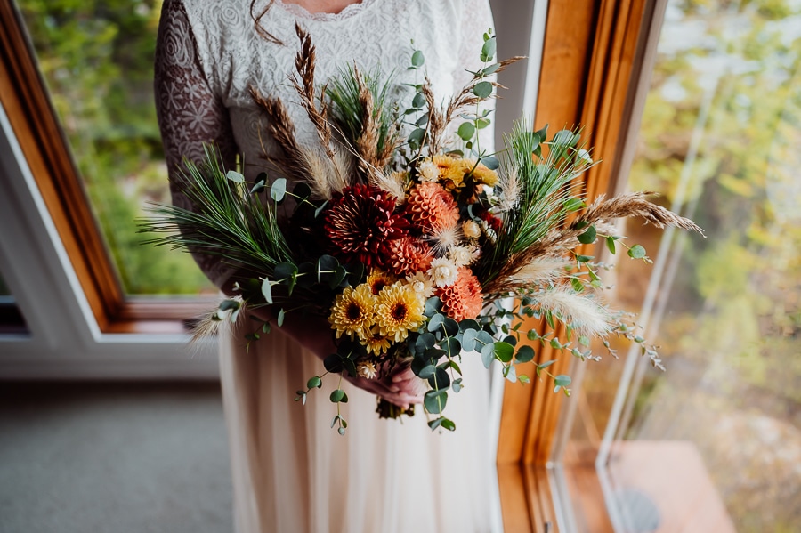 Bride holding wedding bouquet with pine and yellow flowers