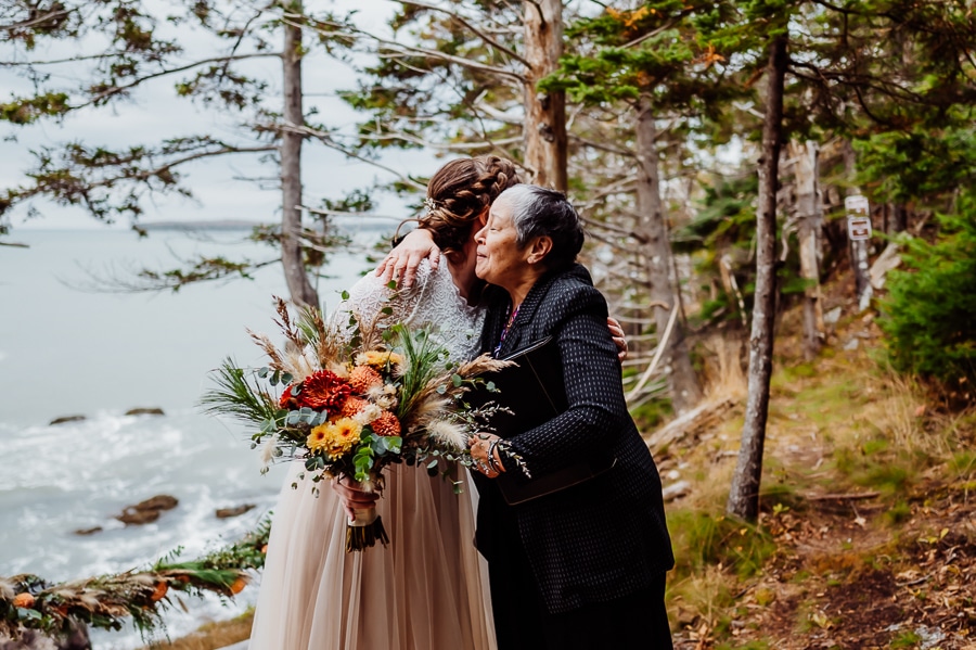 officiant hugging bride next to machiasport ocean cliff