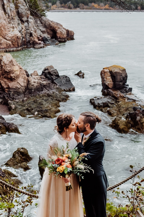 bride and groom kissing in front of ocean side cliffs in machiasport maine