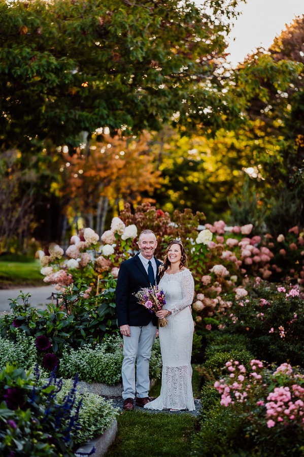Bride and groom smiling together in front of lots of flowers during autumn season