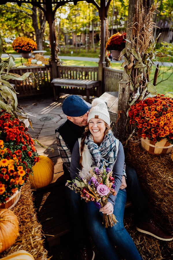 Engaged couple laughing together between fall flowers