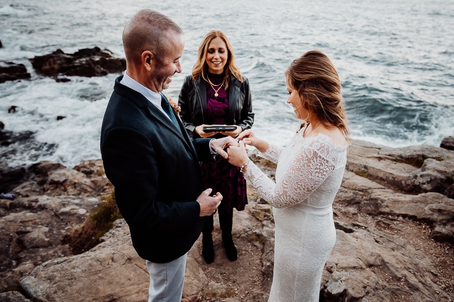 Bride putting ring on grooms finger during elopement ceremony in front of the ocean