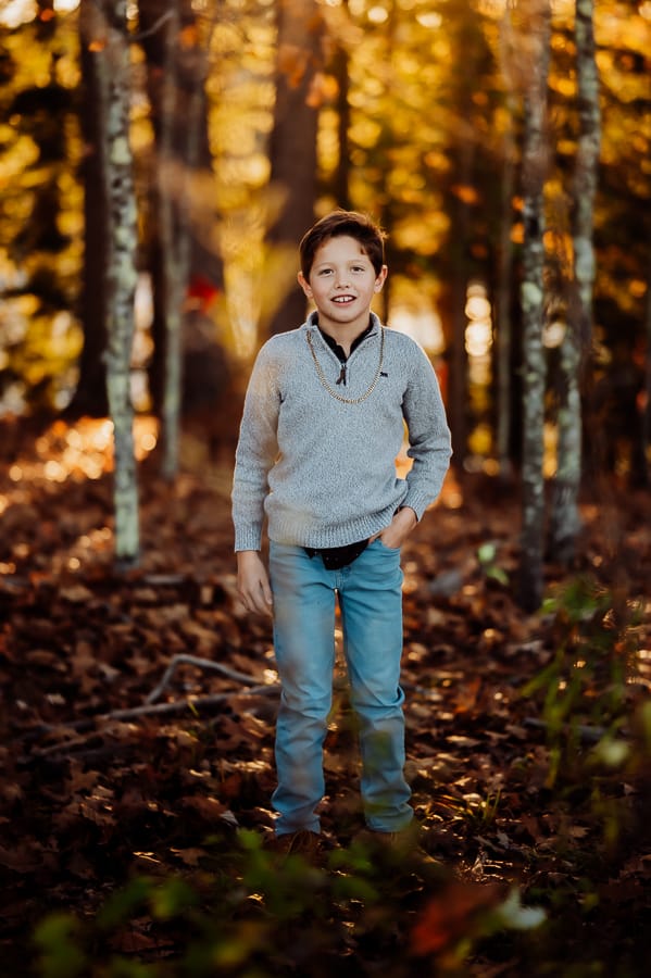 Little boy with brown hair wearing jeans and grey sweater in woods