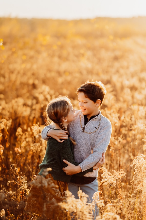 Brother and sister hugging in field of dried autumn bushes